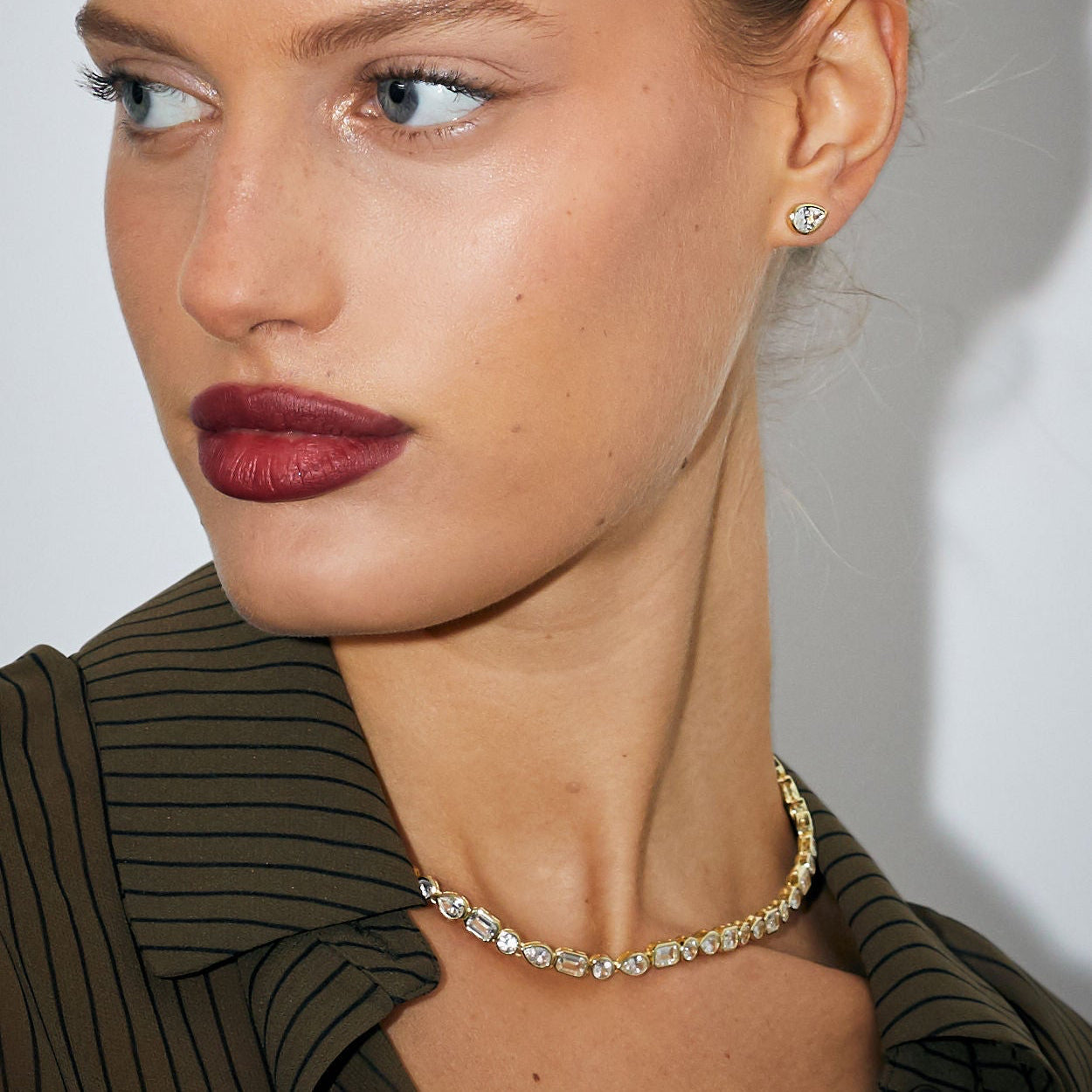 Close-up of a woman wearing a gold necklace and earrings against a neutral background