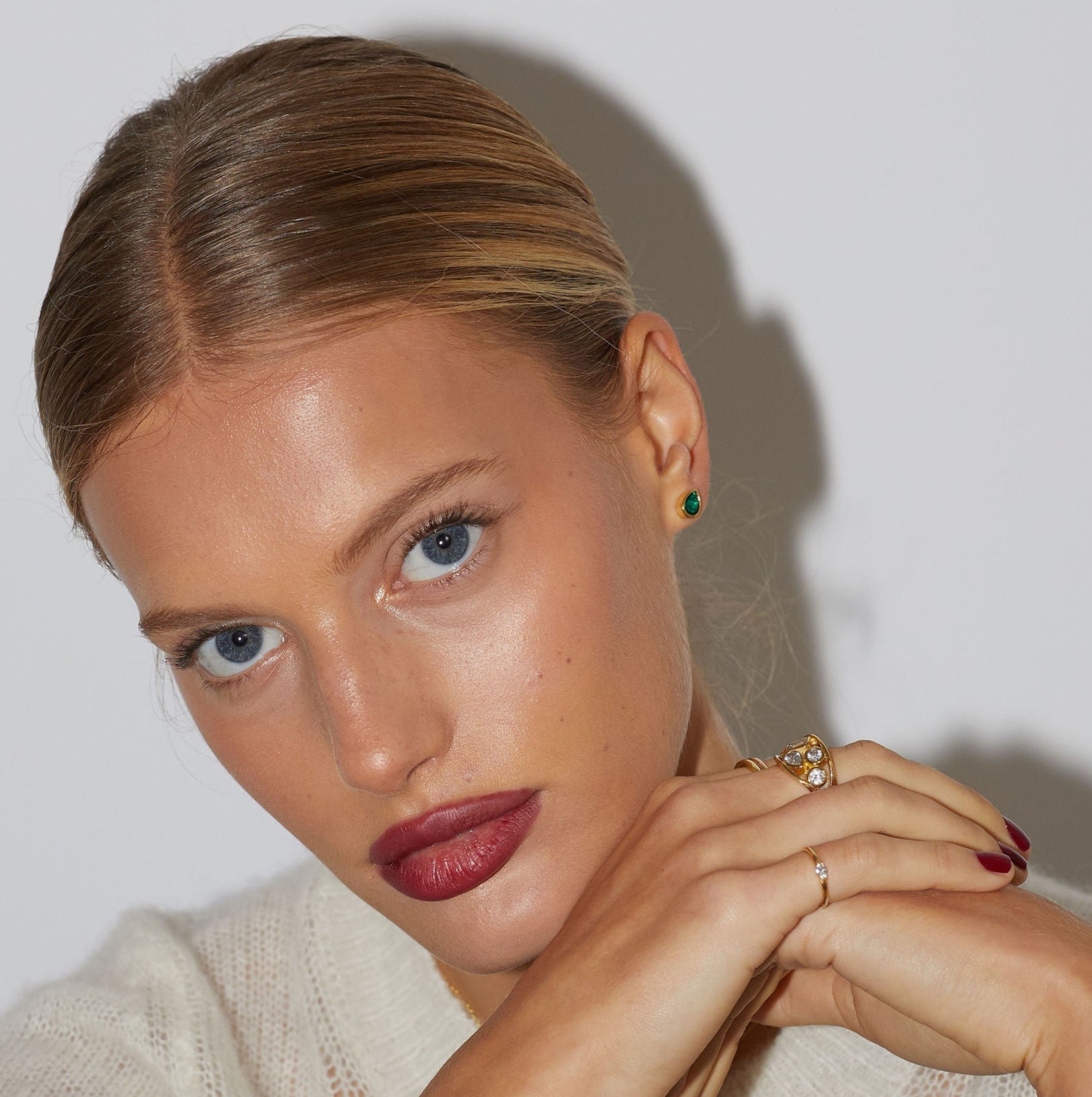 Close-up of a woman with styled hair and jewelry against a neutral background