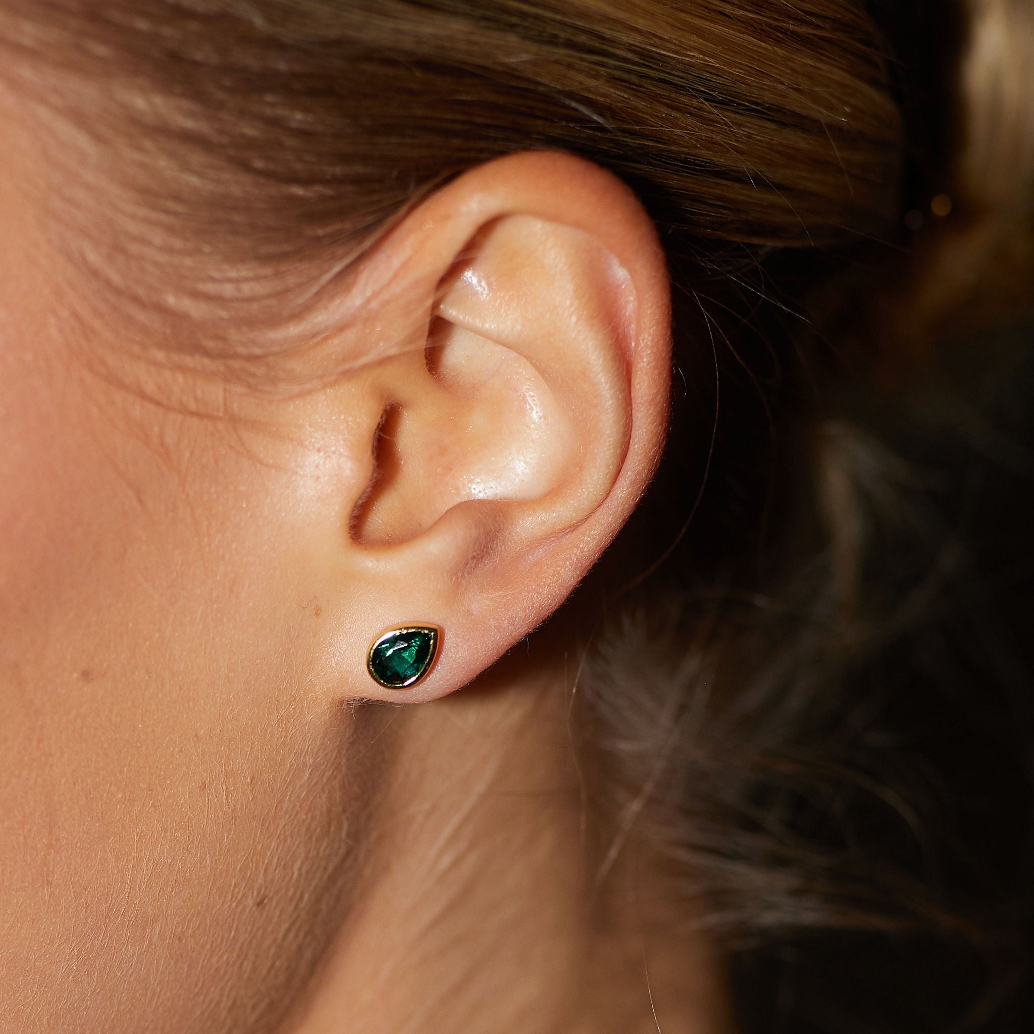 Close-up of an ear wearing a green gemstone earring.