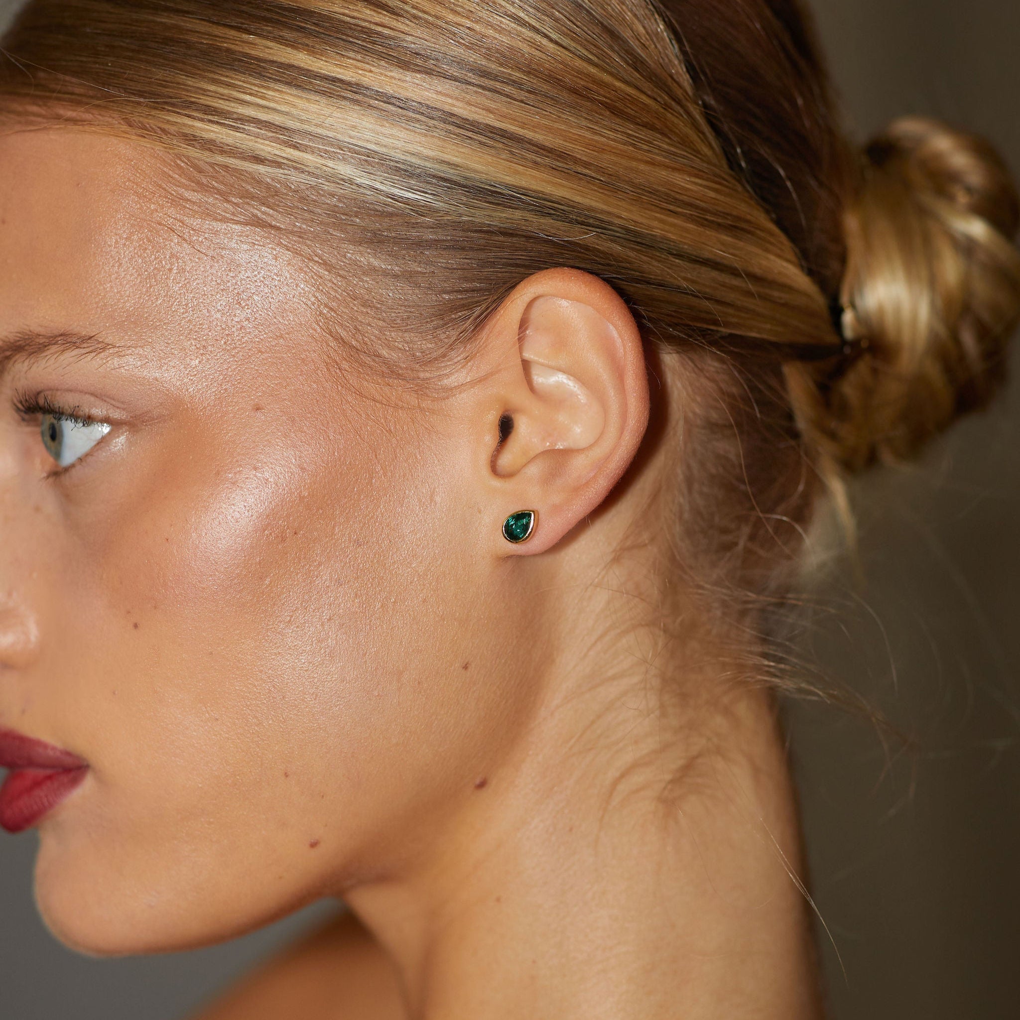 Close-up of a woman's ear with a green earring, hair styled in an updo.
