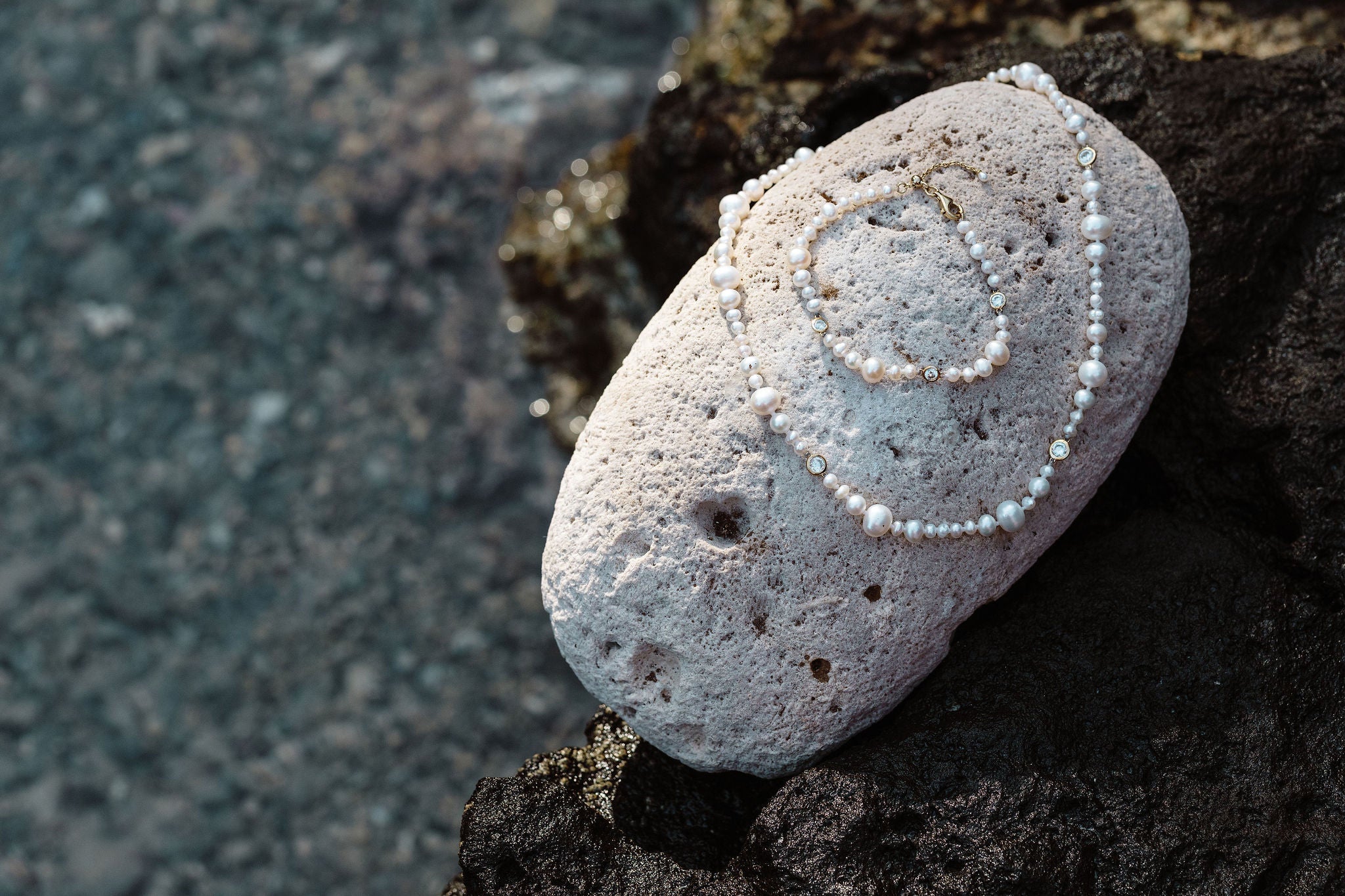 Threaded pearl necklace and bracelet with white sapphires on coral stone by the sea