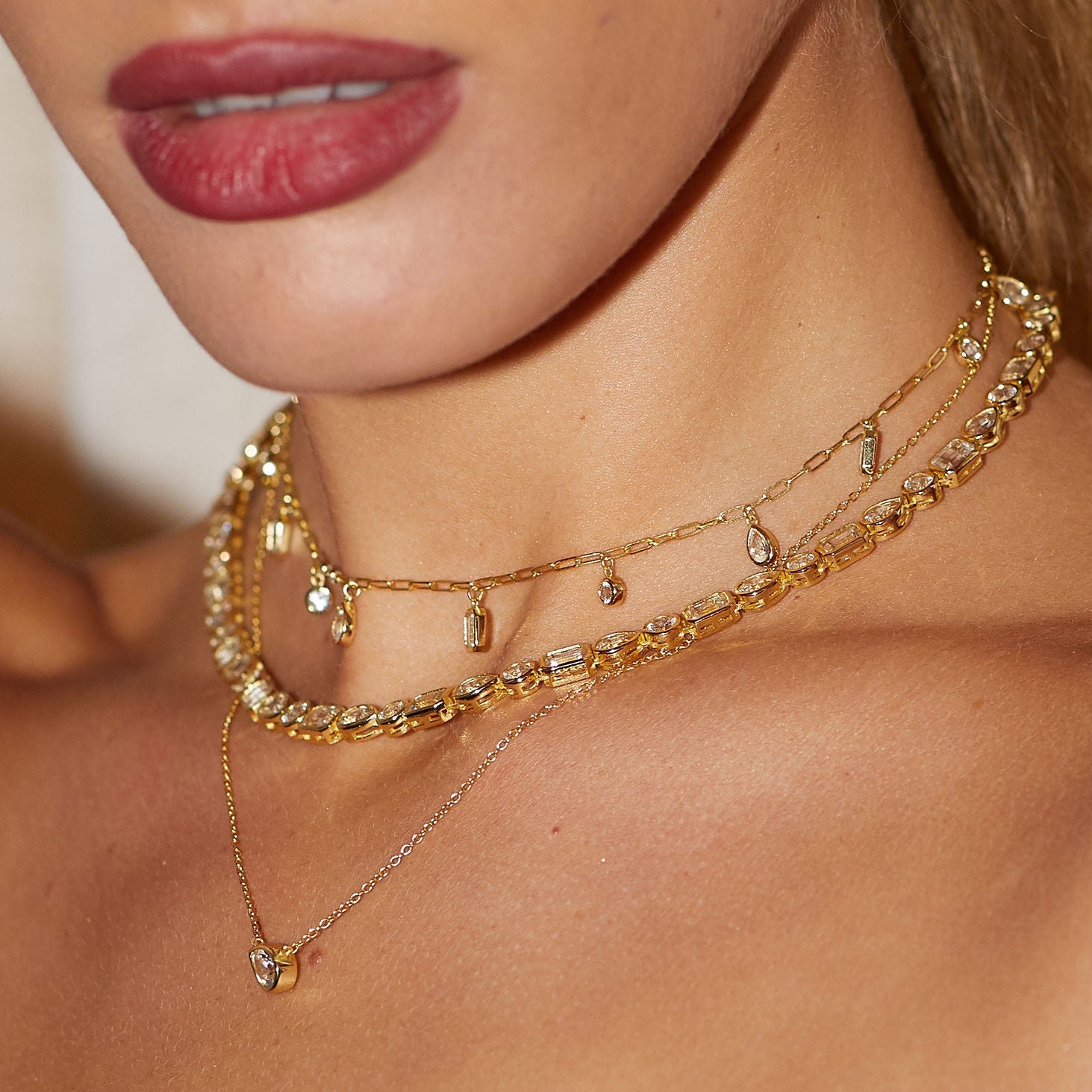 Close-up of a woman wearing multiple gold necklaces with a blurred background