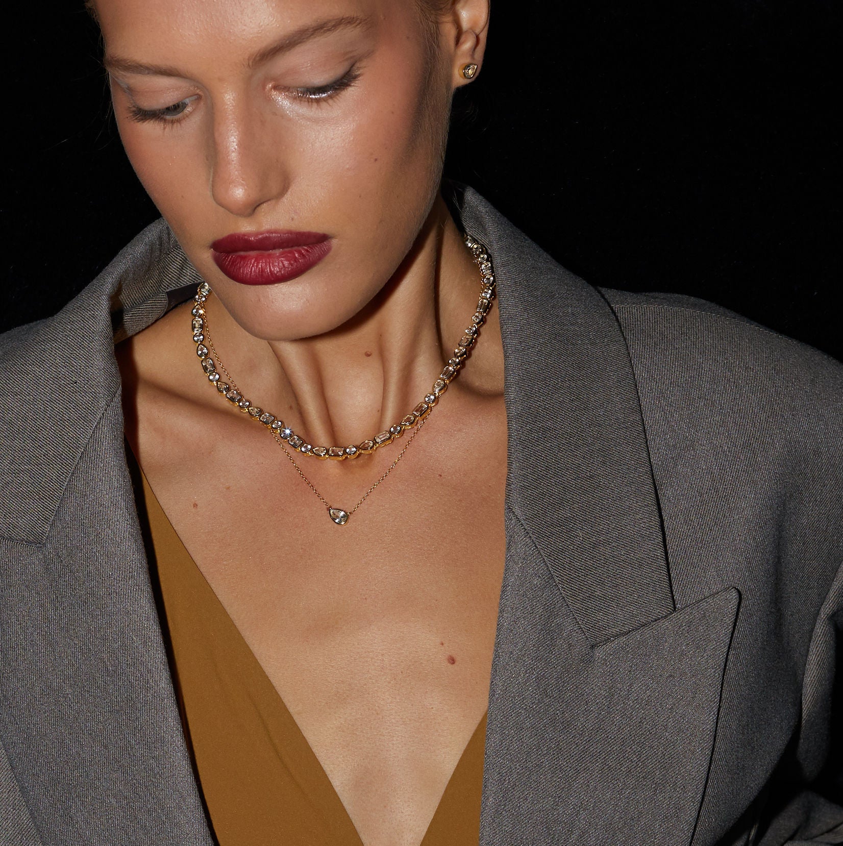 Person wearing a gray blazer over a brown top with a black background