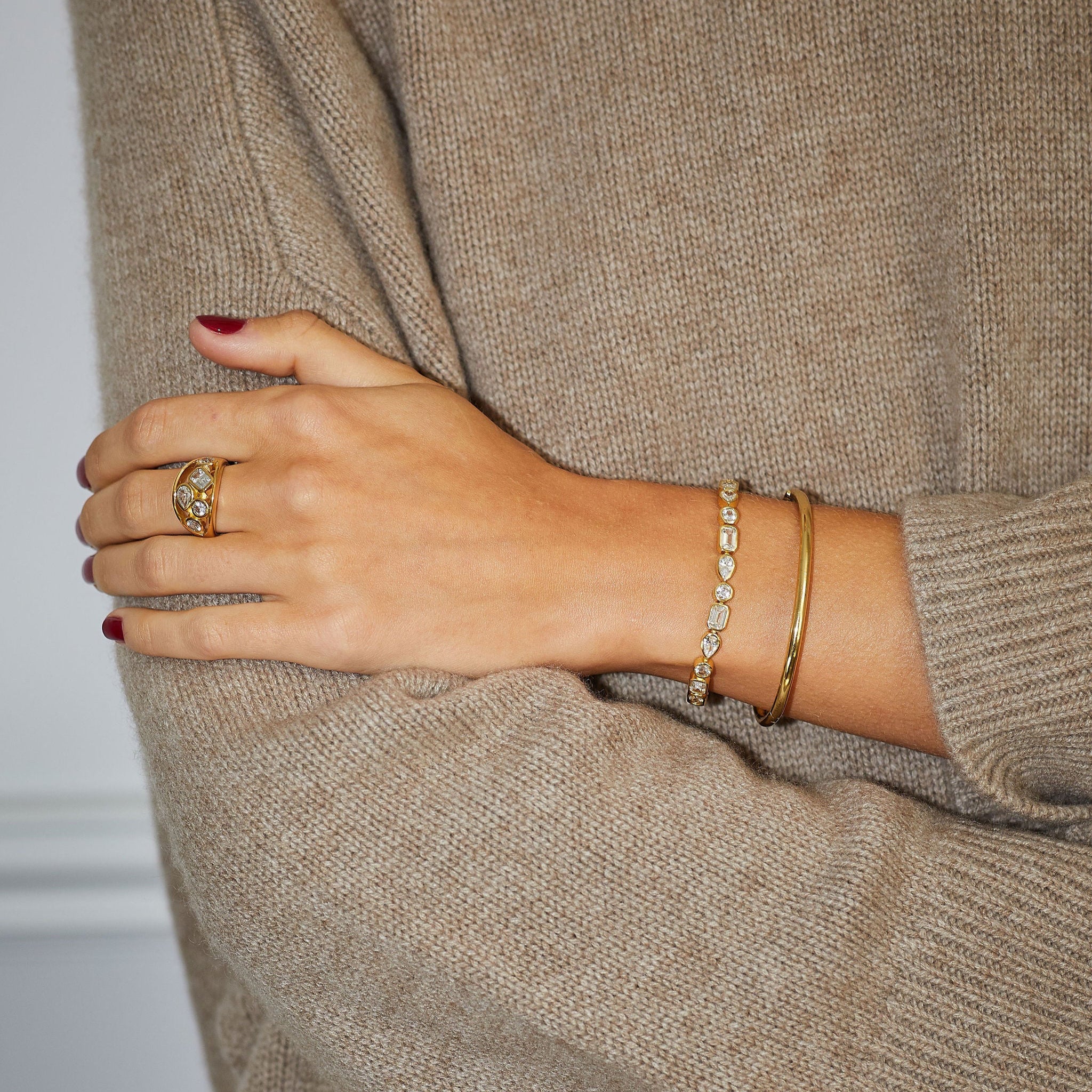 Close-up of a person wearing a beige sweater with jewelry on a neutral background