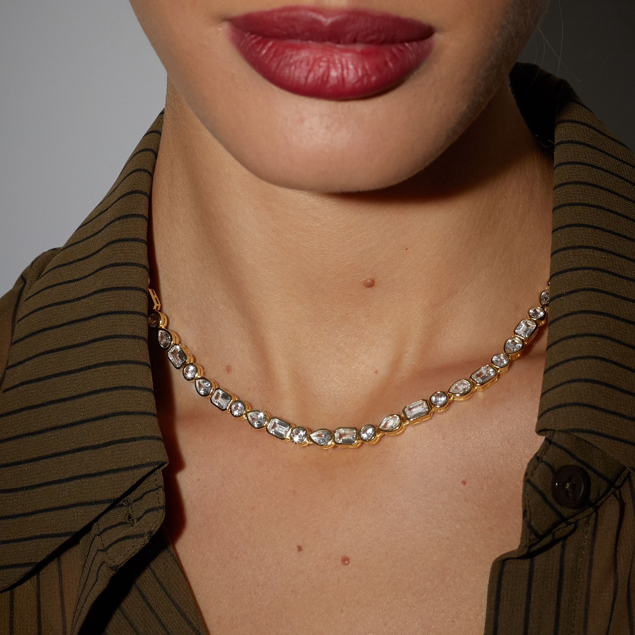 Close-up of a person wearing a gold necklace with a brown striped shirt.